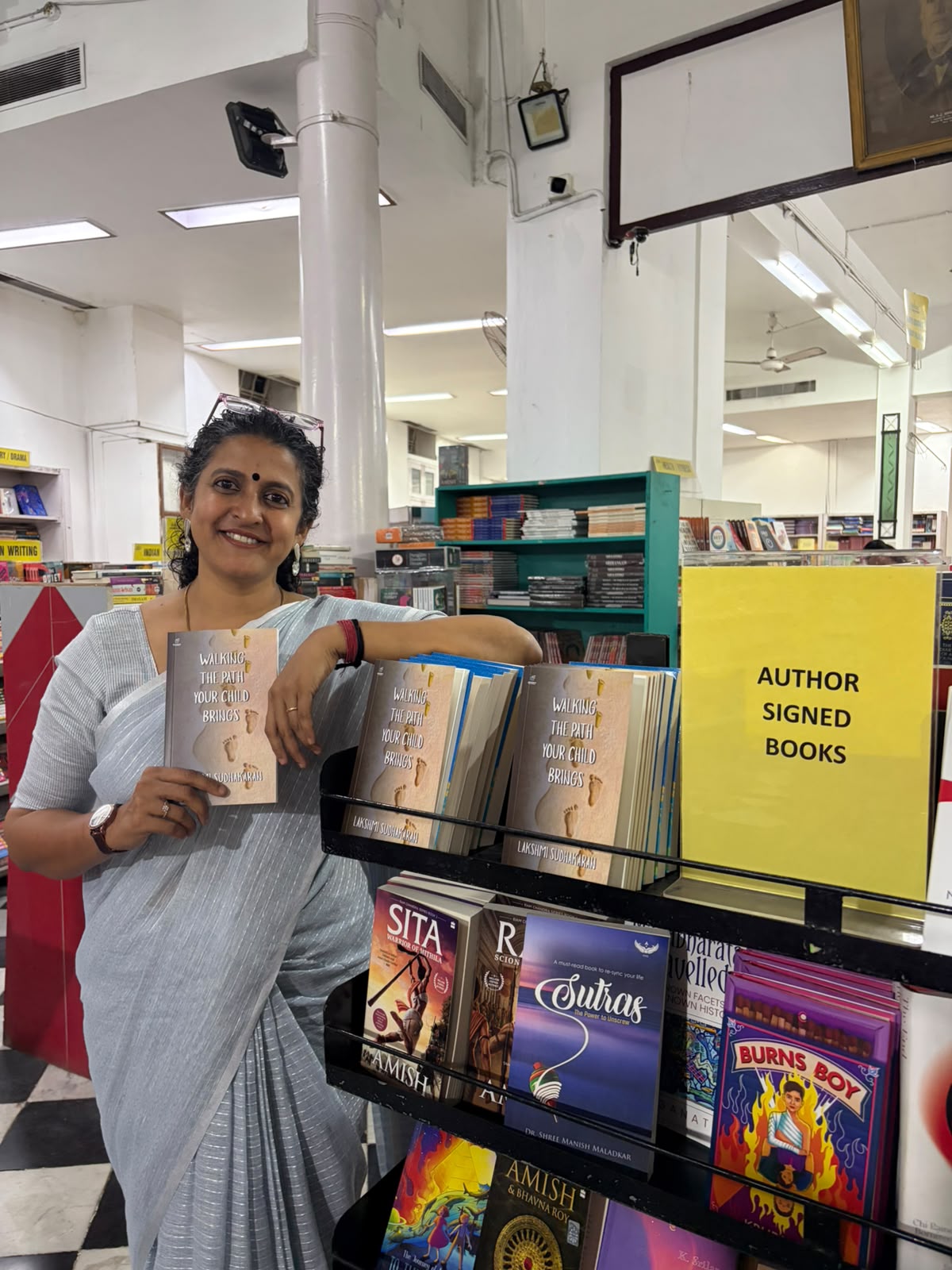 Lakshmi Sudhakaran beside a shelf of author-signed books