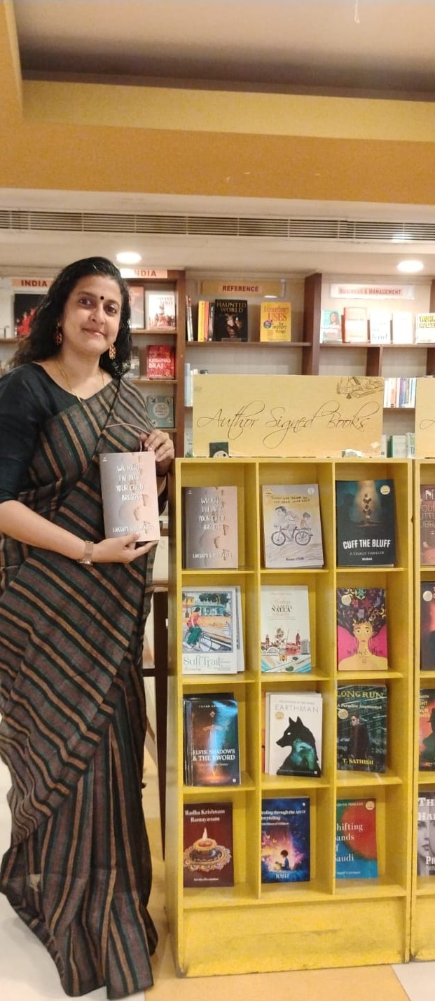 Lakshmi Sudhakaran holding her book beside a bookstore display